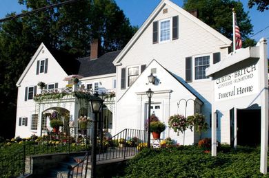 White inn and garden in sunlight with hanging flower baskets and a U.S. flag