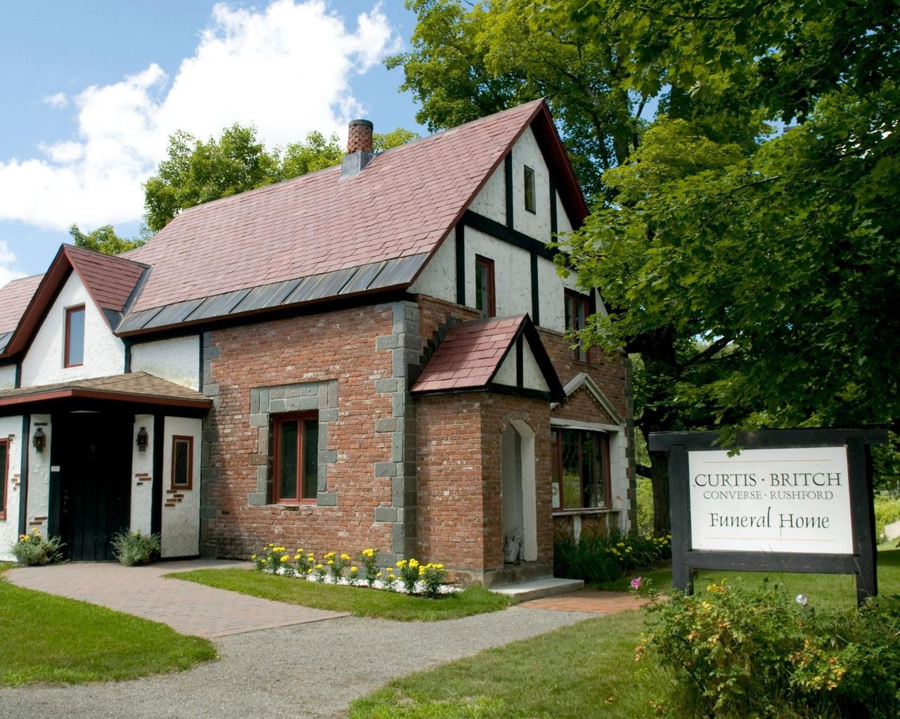 Brick cottage with red roof and garden sign reading “Curtis T…” beside a path