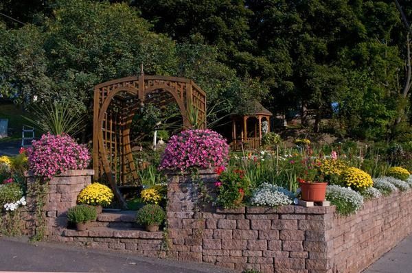 Flower-filled garden with a wooden arbor and stone planters beside a path