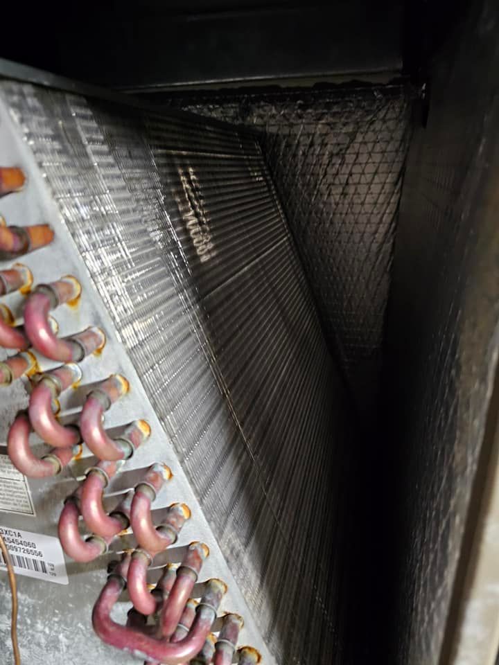 A-coil inside an HVAC system with visible dust buildup on the fins and surrounding surfaces.