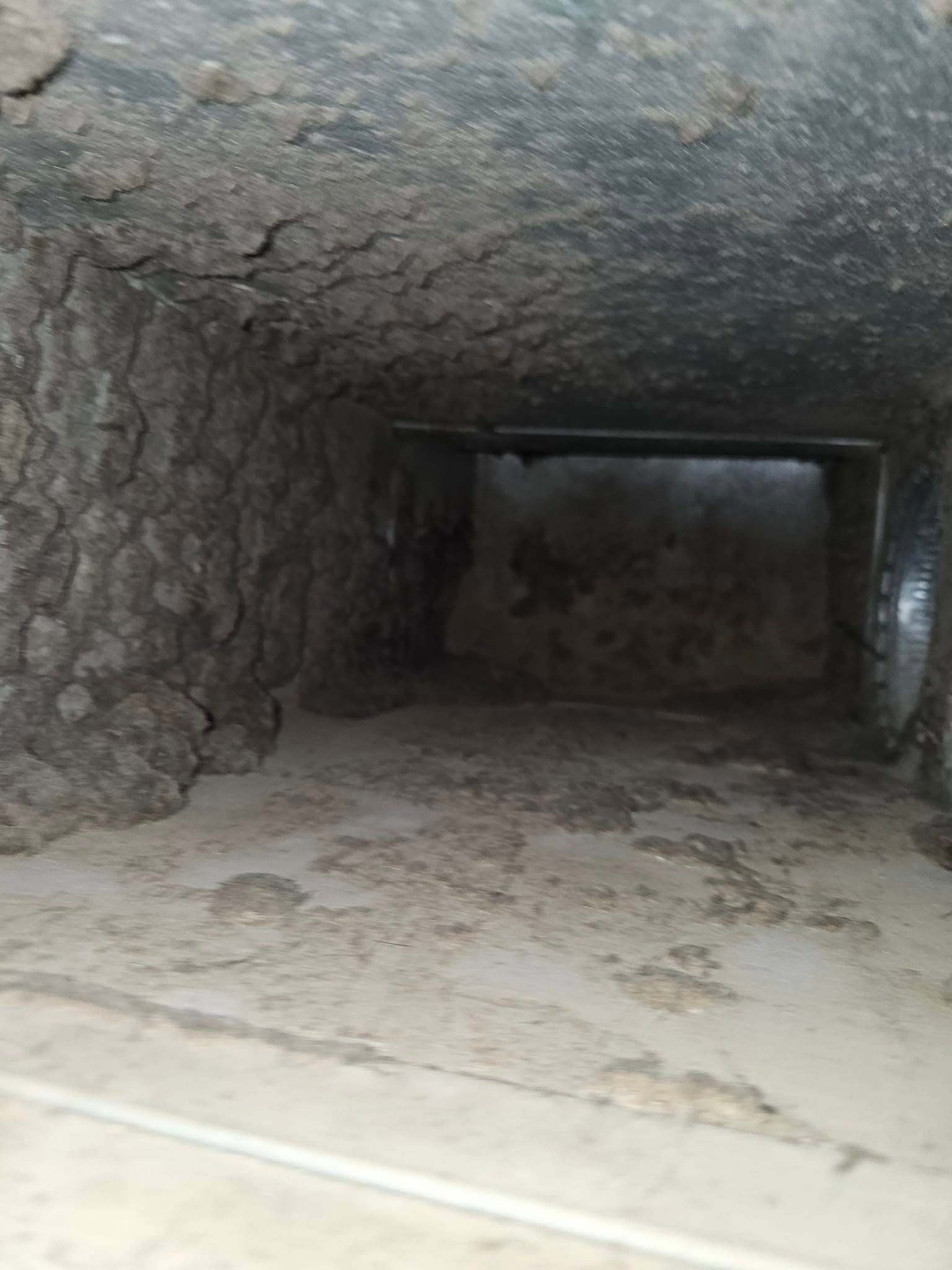 Dust-covered interior of an air duct showing heavy buildup on the walls and floor.