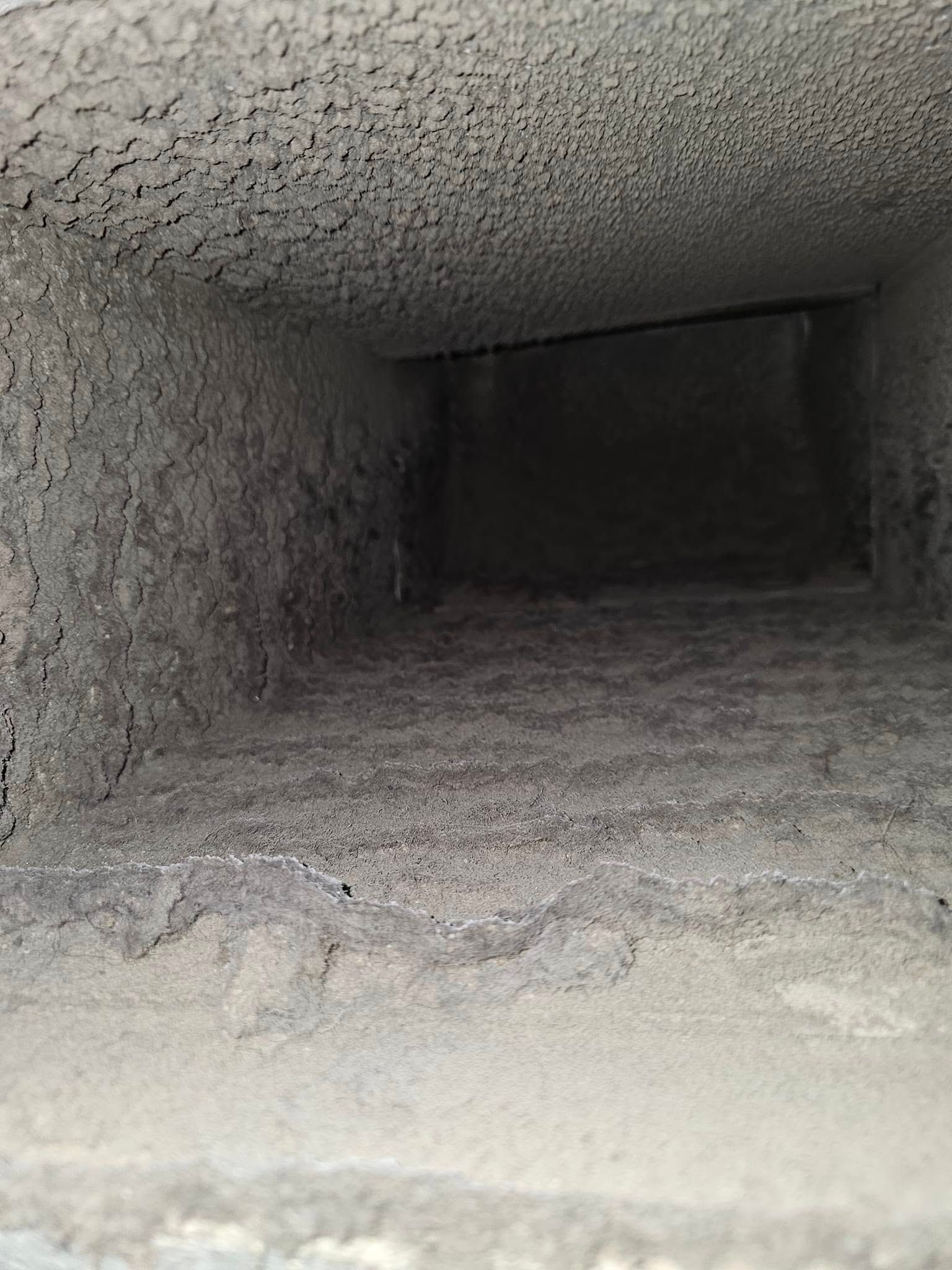 Air duct interior heavily coated with thick dust buildup on the walls and floor.