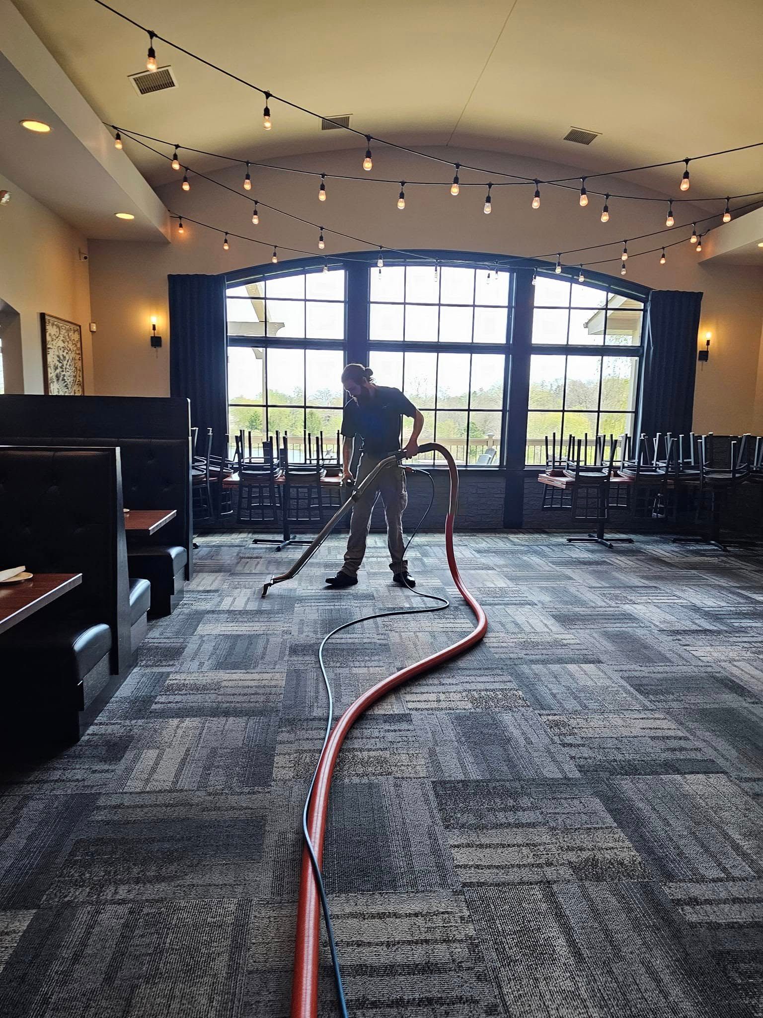 Technician providing commercial carpet cleaning service in restaurant dining area with professional equipment