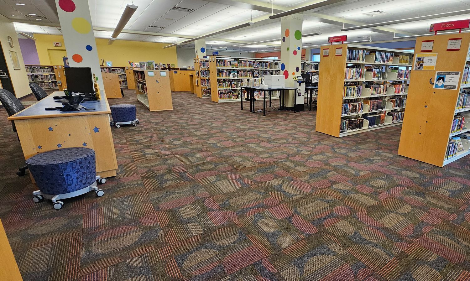 Commercial carpet cleaning in public library showing freshly cleaned carpet tiles and organized shelving area