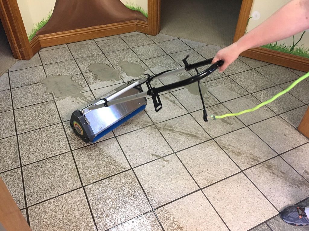 Commercial tile and grout cleaning in progress with professional floor scrubbing equipment on stained tile flooring.