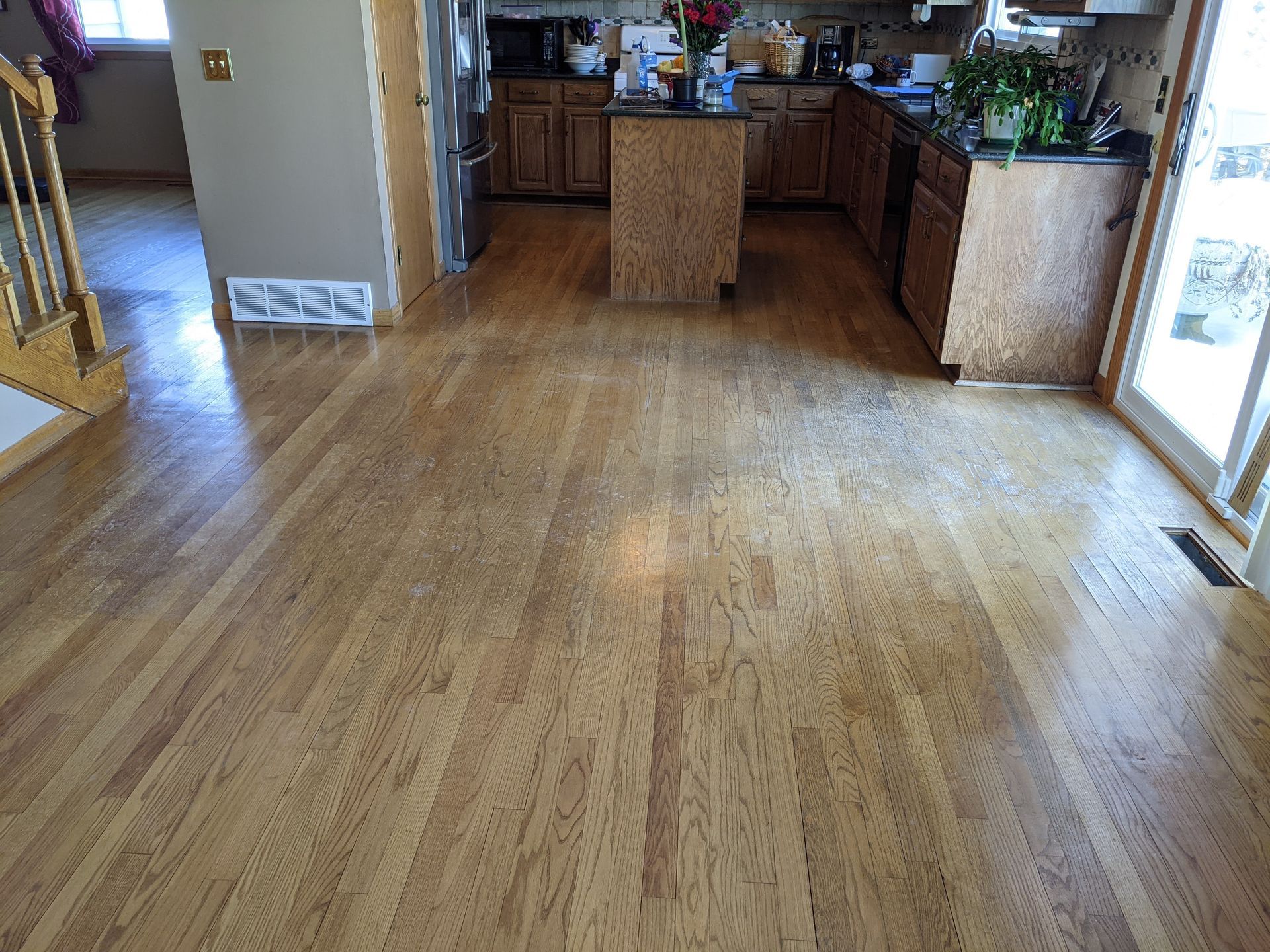 Hardwood kitchen floor before professional cleaning showing buildup and wear in high traffic areas