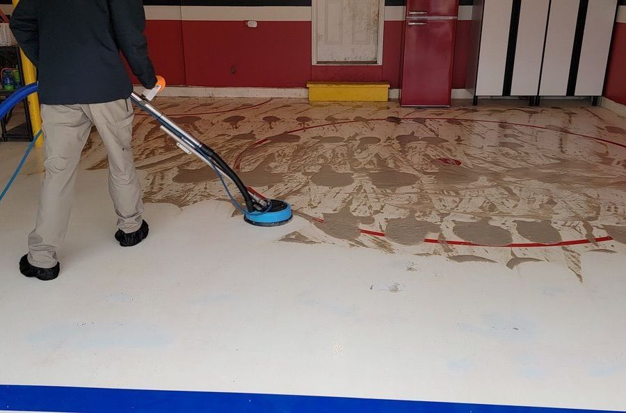 Technician cleaning commercial concrete floor with professional surface cleaning equipment in garage space