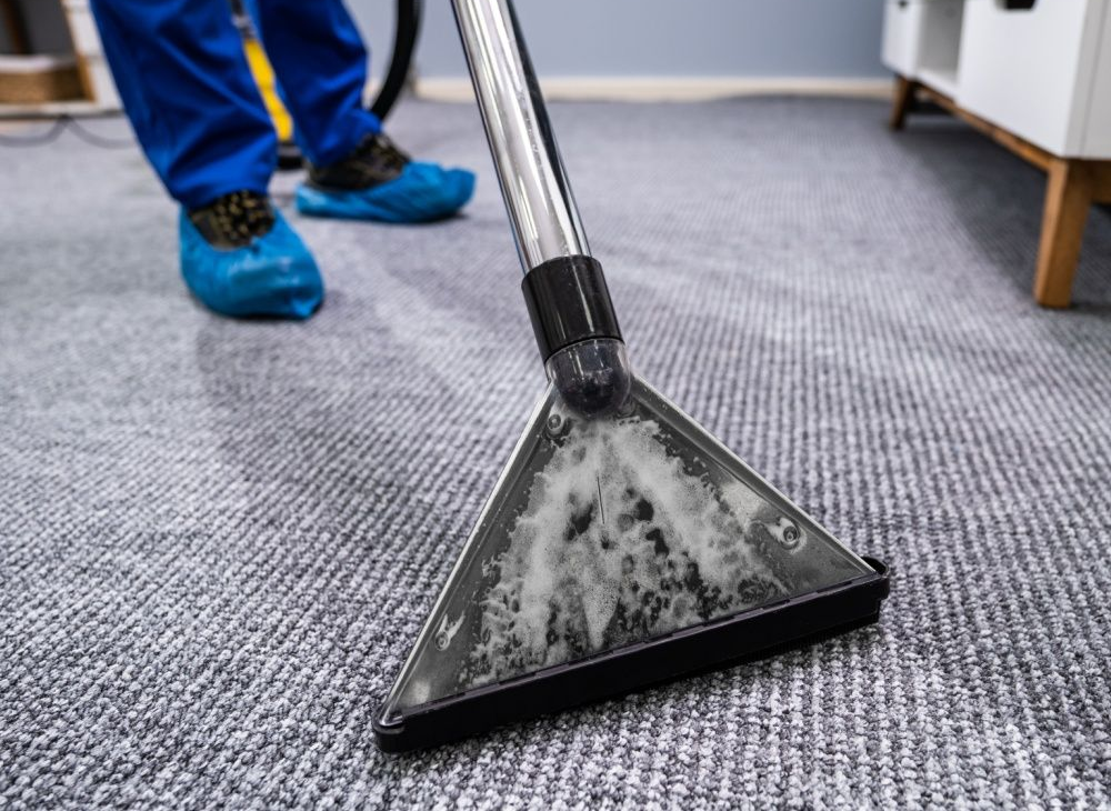 Carpet cleaning tool on gray carpet, with worker’s blue shoes visible nearby