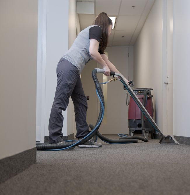 Person vacuuming a carpeted hallway with a canister vacuum cleaner