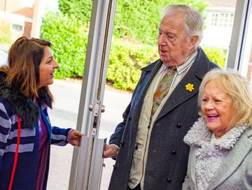 A woman is opening a door for an elderly couple.