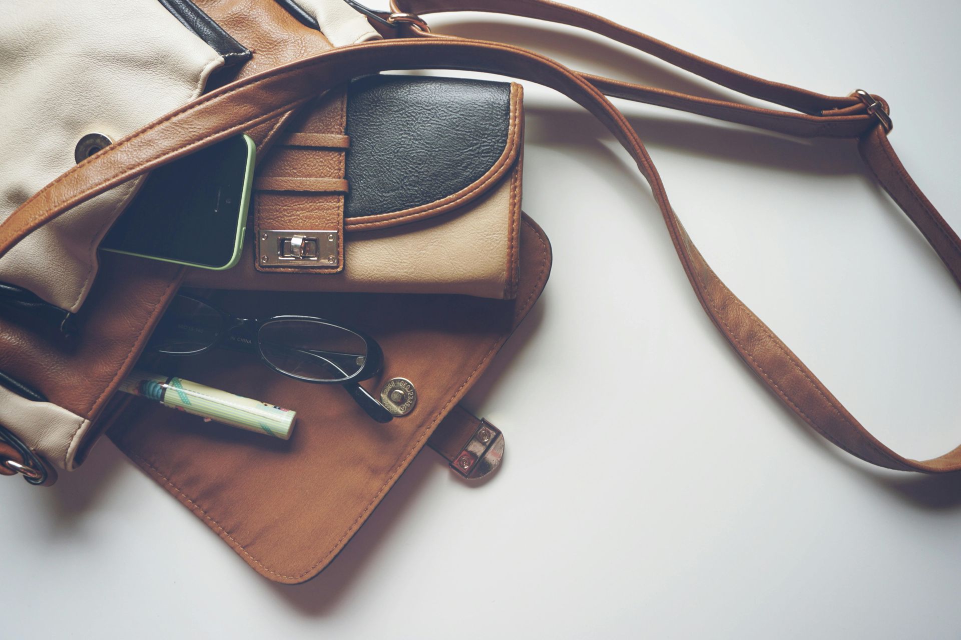 A brown purse with a cell phone , wallet , glasses , and lipstick in it.