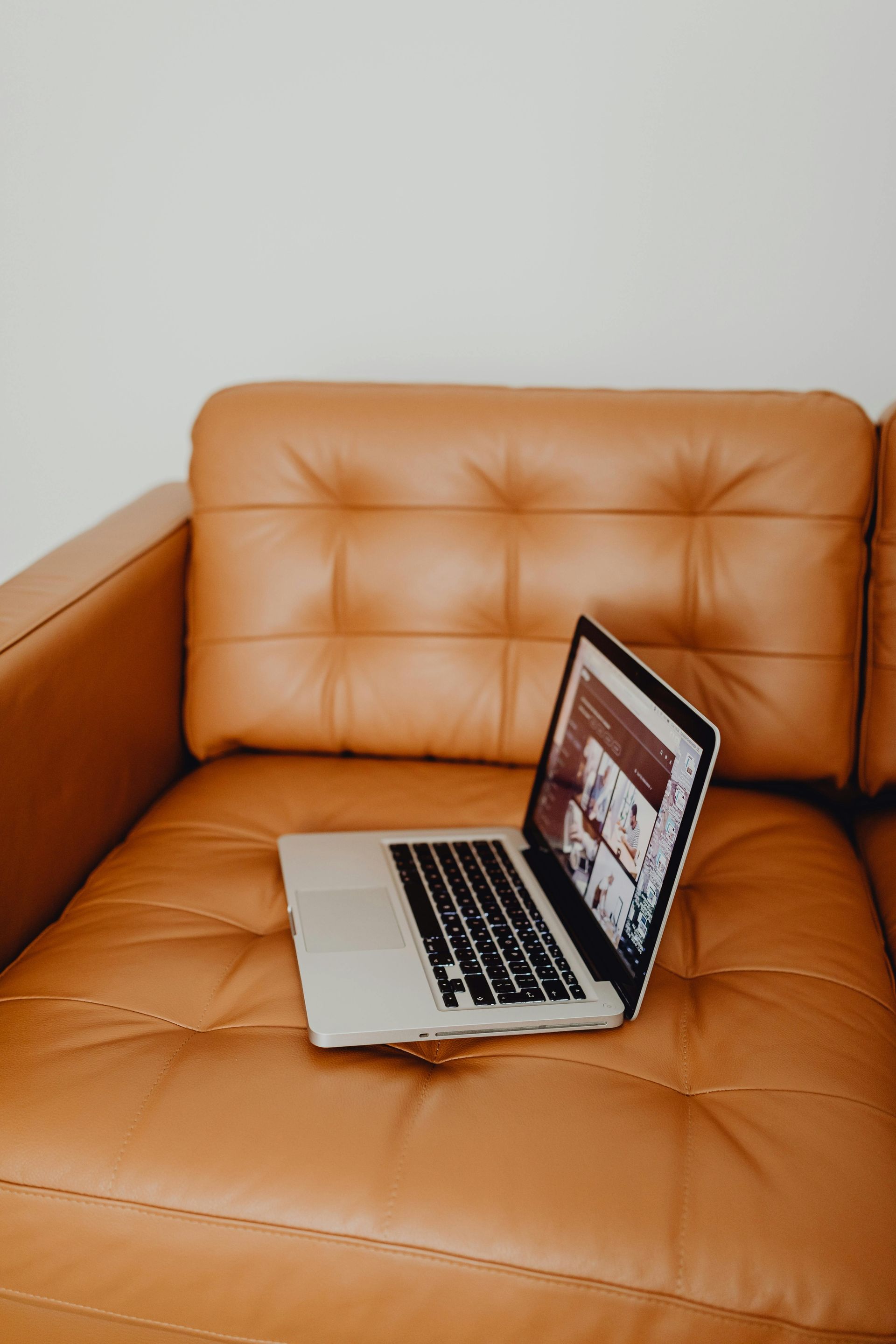 A laptop is sitting on a brown leather couch.