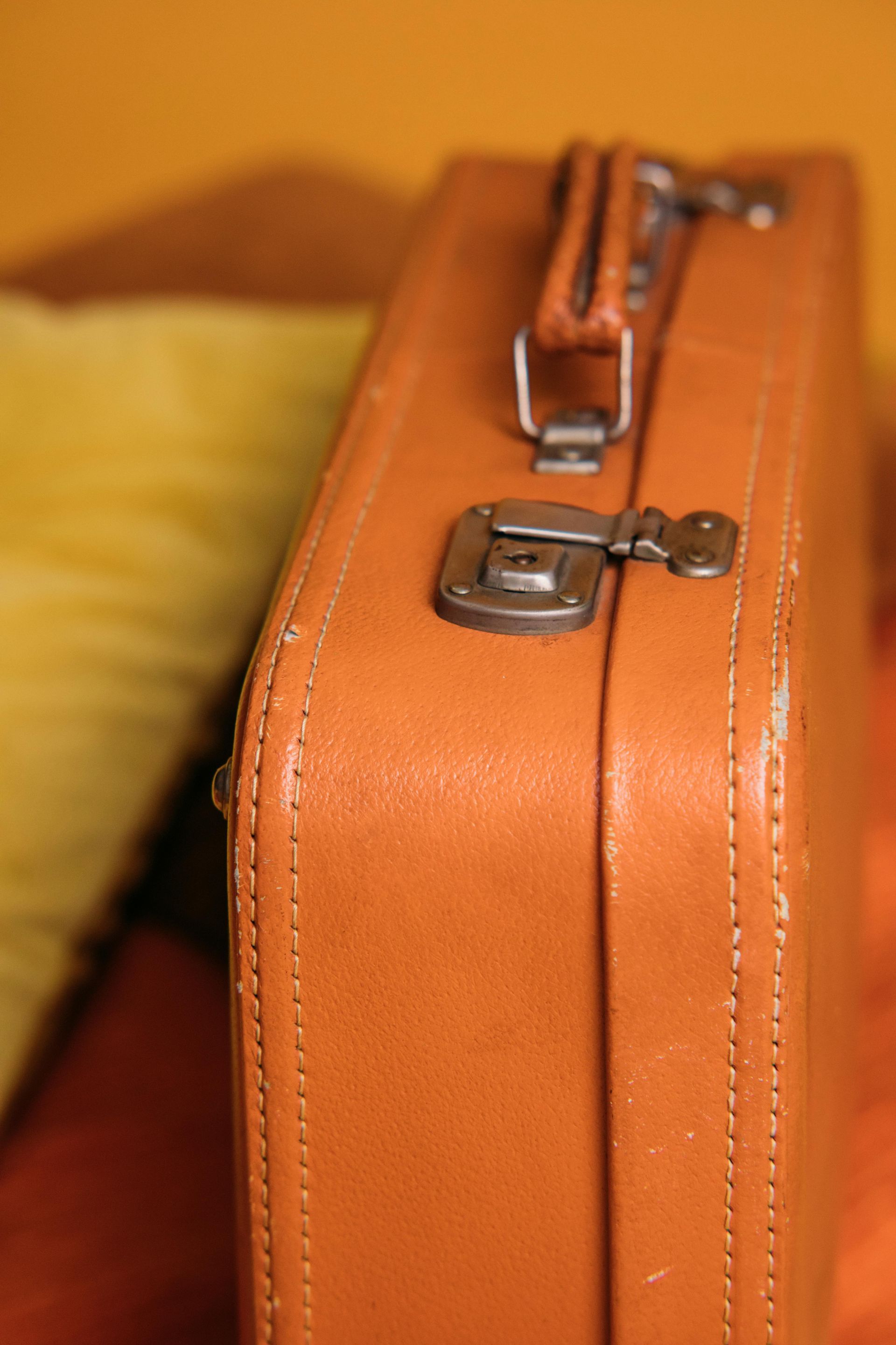 A brown suitcase is sitting on a table next to a yellow pillow.