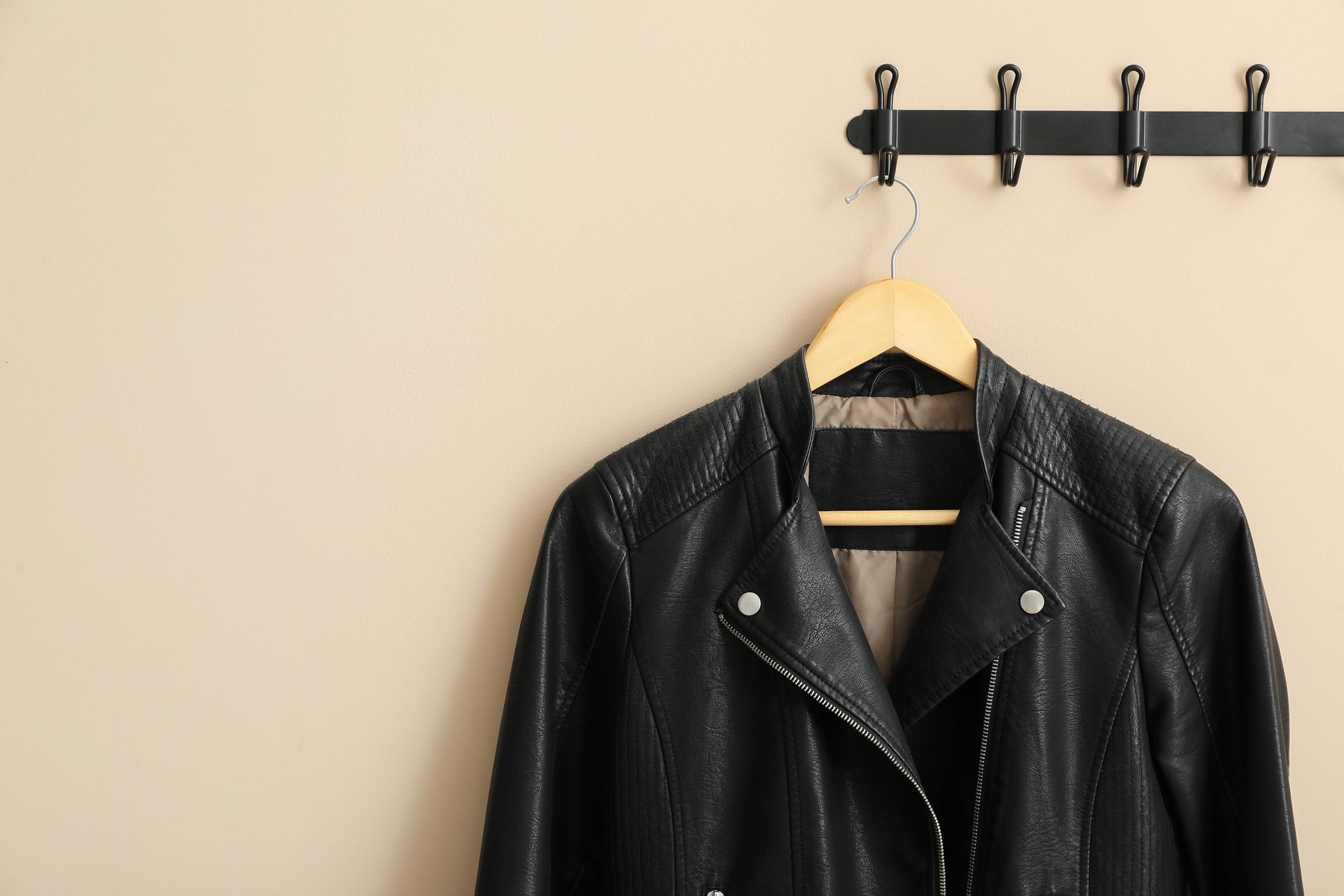 A black leather jacket is hanging on a hook on a wall.