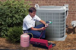 Technician servicing an outdoor HVAC unit beside a brick wall, with tools and a gas cylinder nearby