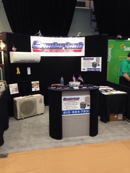 Trade show booth with black table, banner sign, brochures, and white air conditioner display on a carpeted floor
