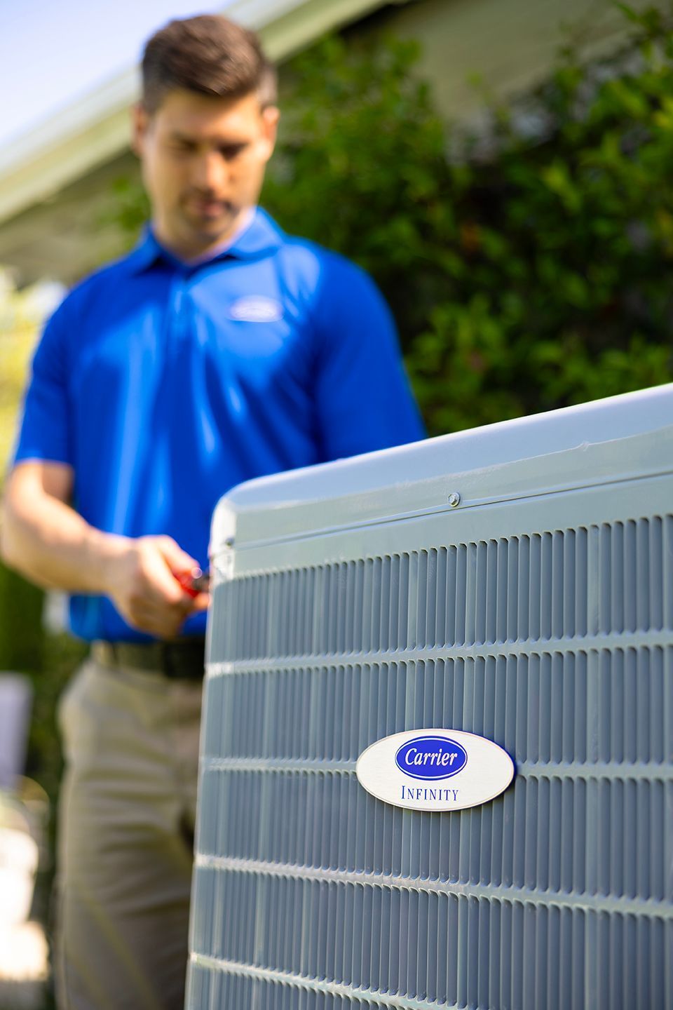 Technician in blue shirt inspecting outdoor air conditioner unit outside a home