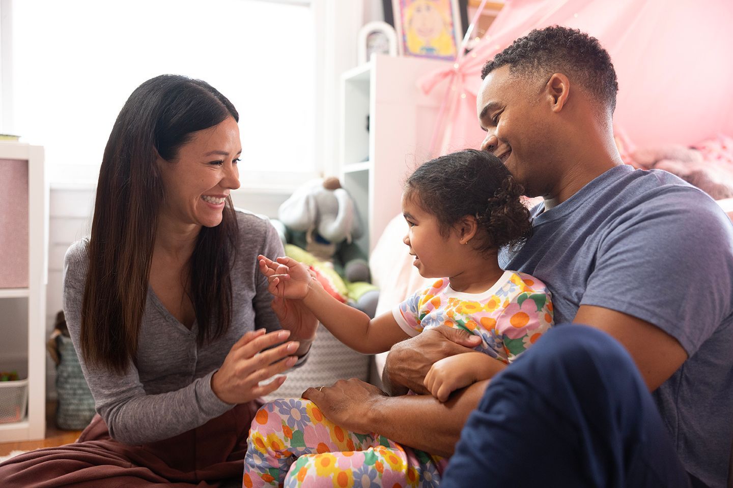 Family sitting on a couch, smiling as parents admire a baby holding a small object.