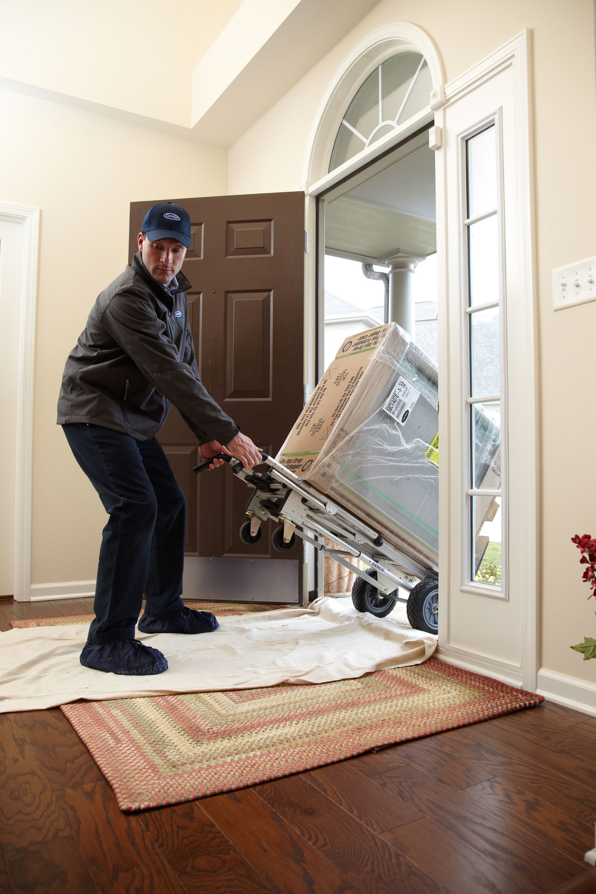 Man maneuvering a wrapped chair dolly through a doorway onto a rug in a foyer