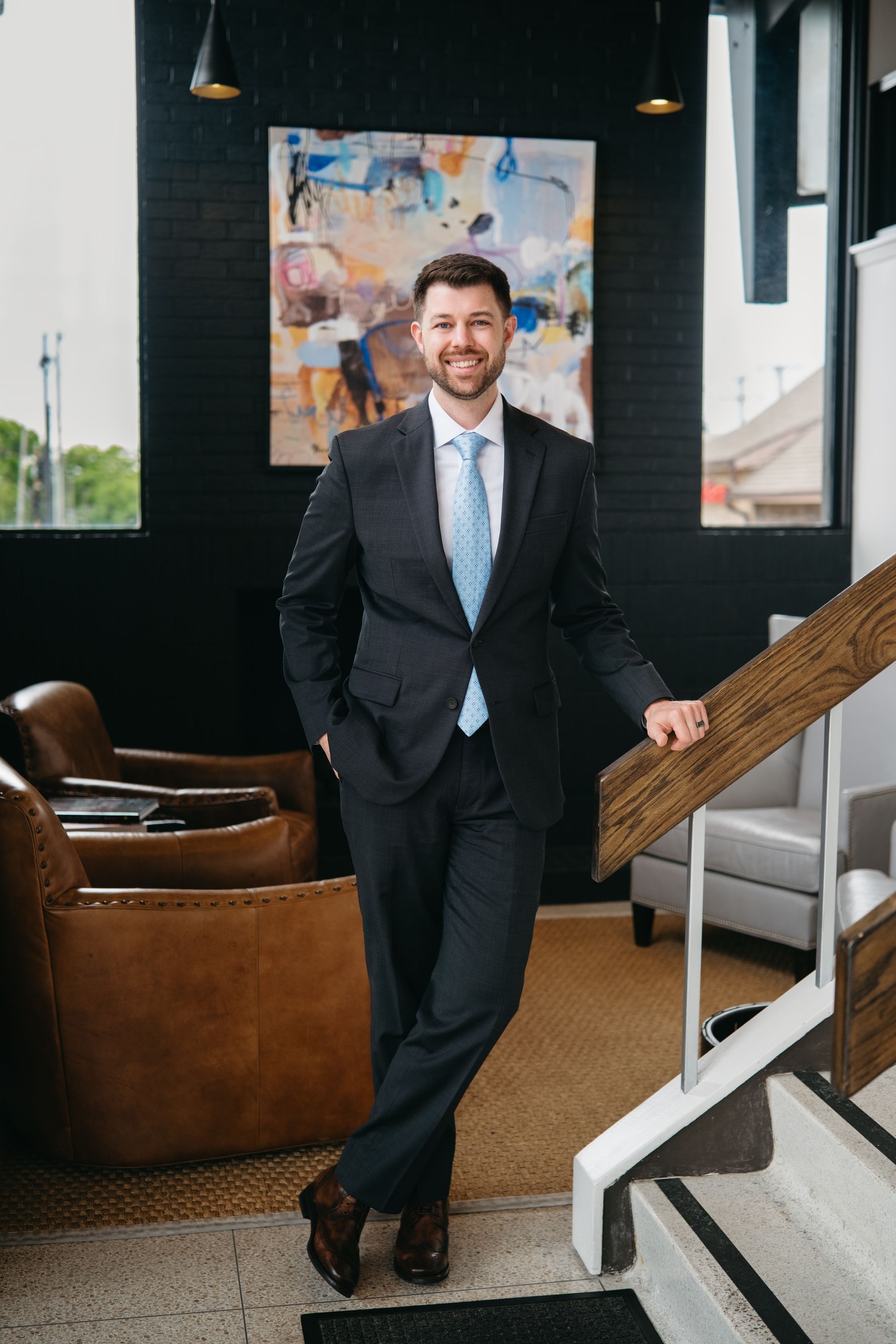 Jackson Wagner standing at the bottom of a staircase, smiling and wearing a dark suit.