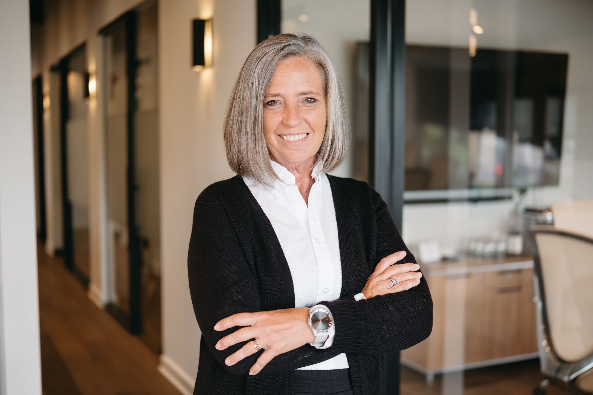 Jennifer Lamb headshot. A woman with short hair and her arms crossed, smiling and wearing a white shirt and black cardigan.