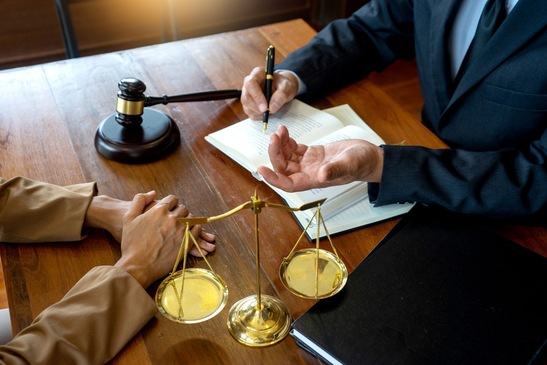 Lawyers signing documents at a desk with a brass scale of justice and gavel