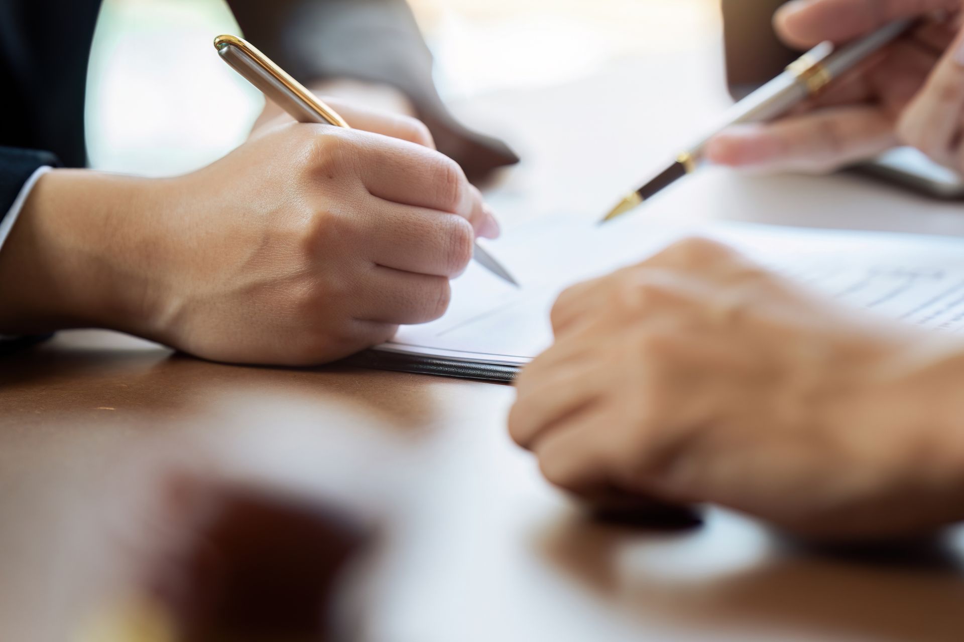 Hands holding pens over a notebook during a meeting or discussion