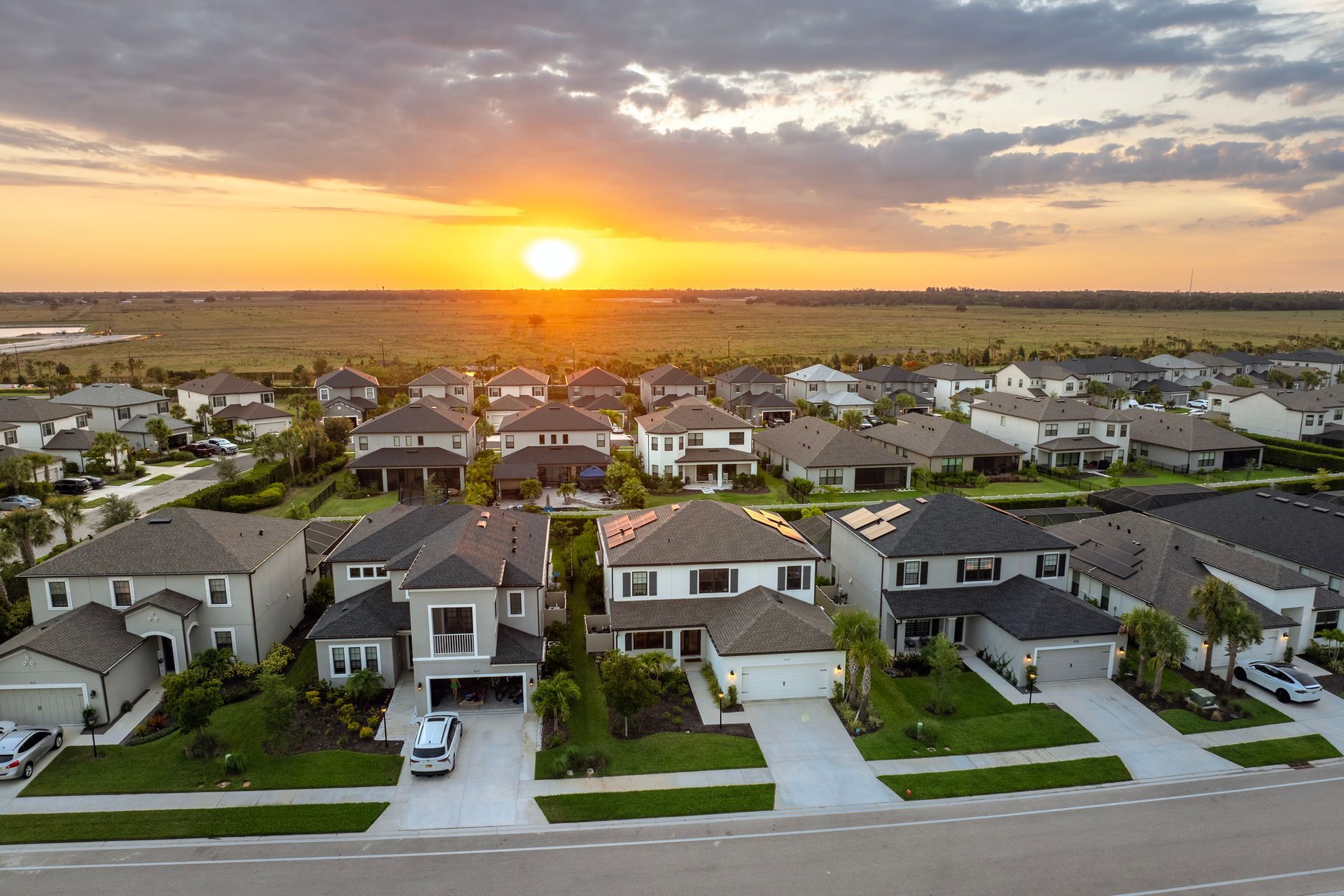 Suburban neighborhood at sunset with rows of modern houses and a glowing orange sky