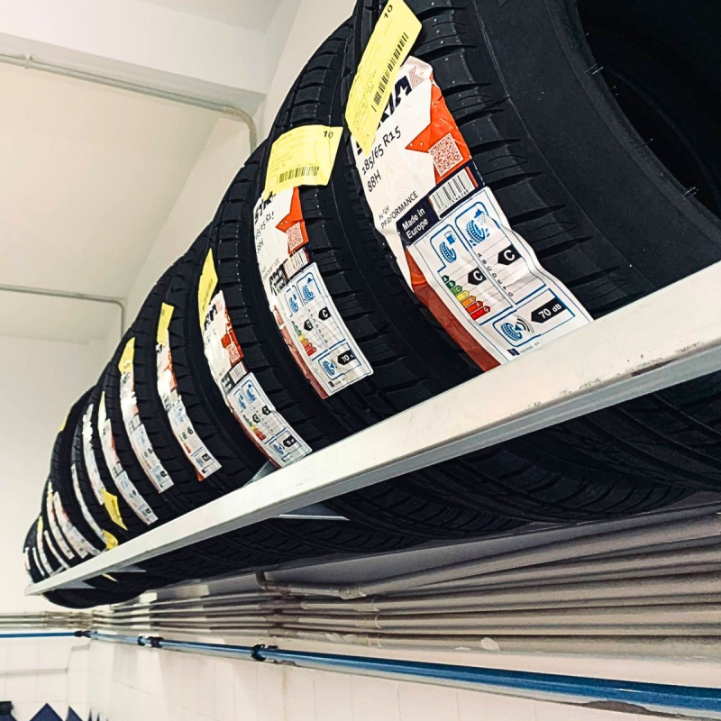 Una fila di pneumatici neri con etichette di prodotto esposti su uno scaffale di un magazzino.