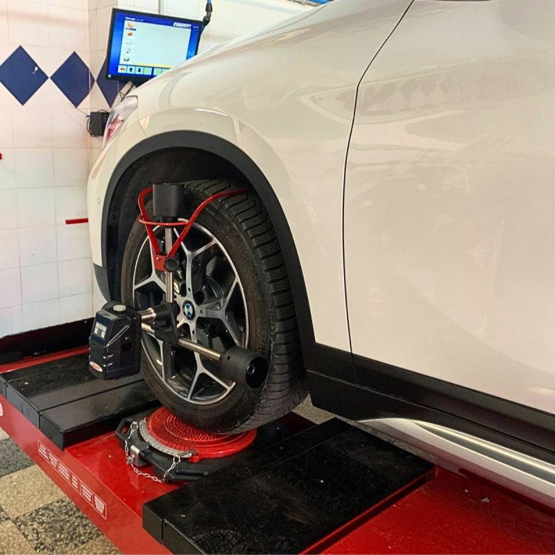 Ruota di un'auto su una macchina per l'allineamento in un'officina, con apparecchiatura di rilevamento collegata.