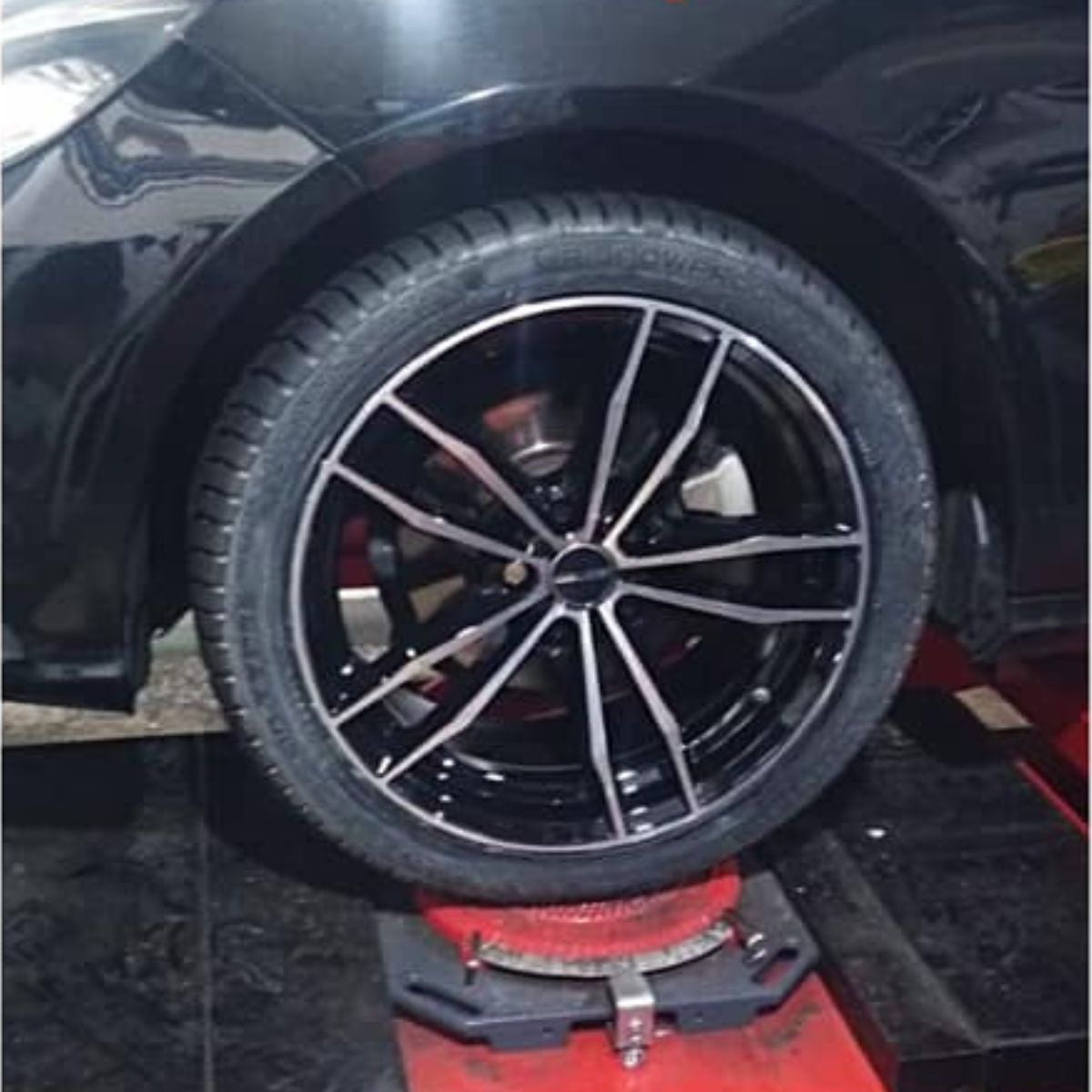Ruota nera per auto su un ponte sollevatore rosso in un garage, che mostra un cerchione in lega sportivo e uno pneumatico.