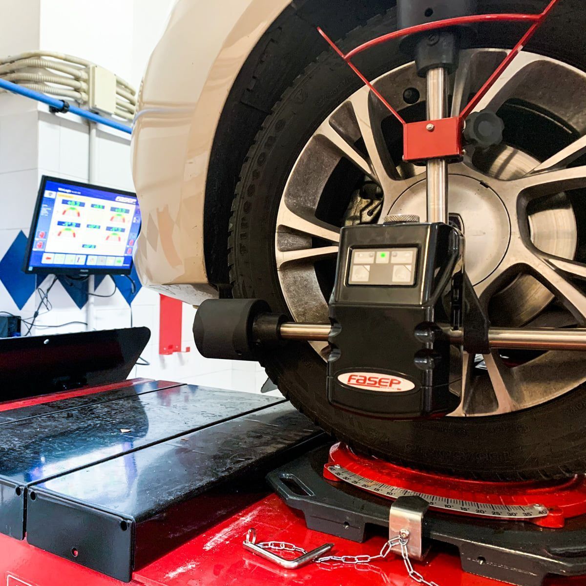 Ruota di un'auto su una macchina per l'allineamento in un'officina, con monitor e braccio di misurazione rosso collegato.