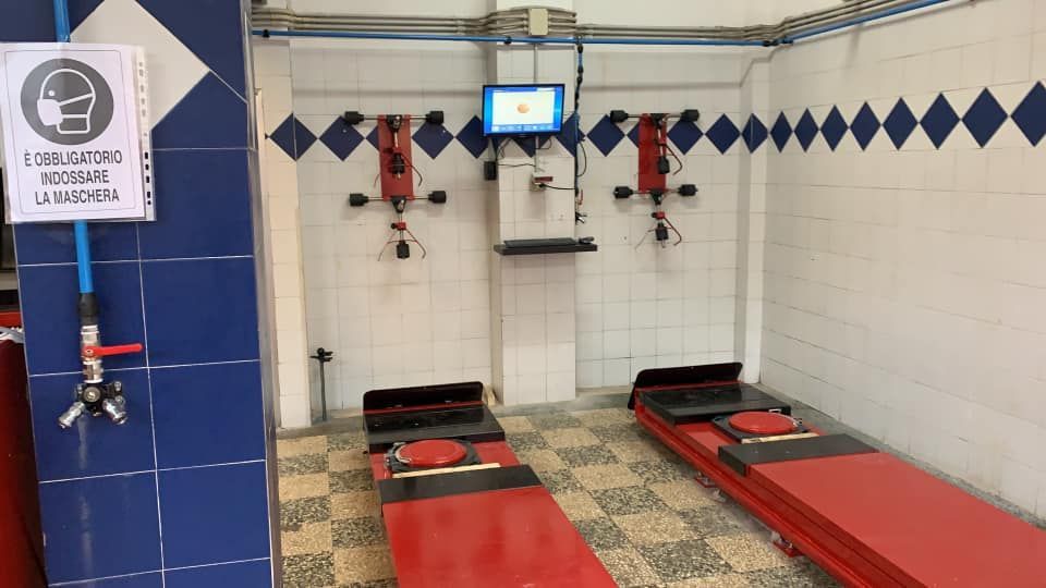 Bagno con piastrelle bianche, panche rosse, soffione a parete, dettagli blu e monitor centrale.