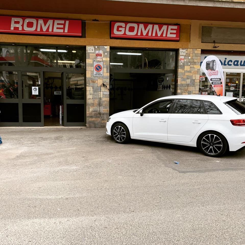 Auto bianca parcheggiata fuori da un gommista con cartelli rossi con la scritta