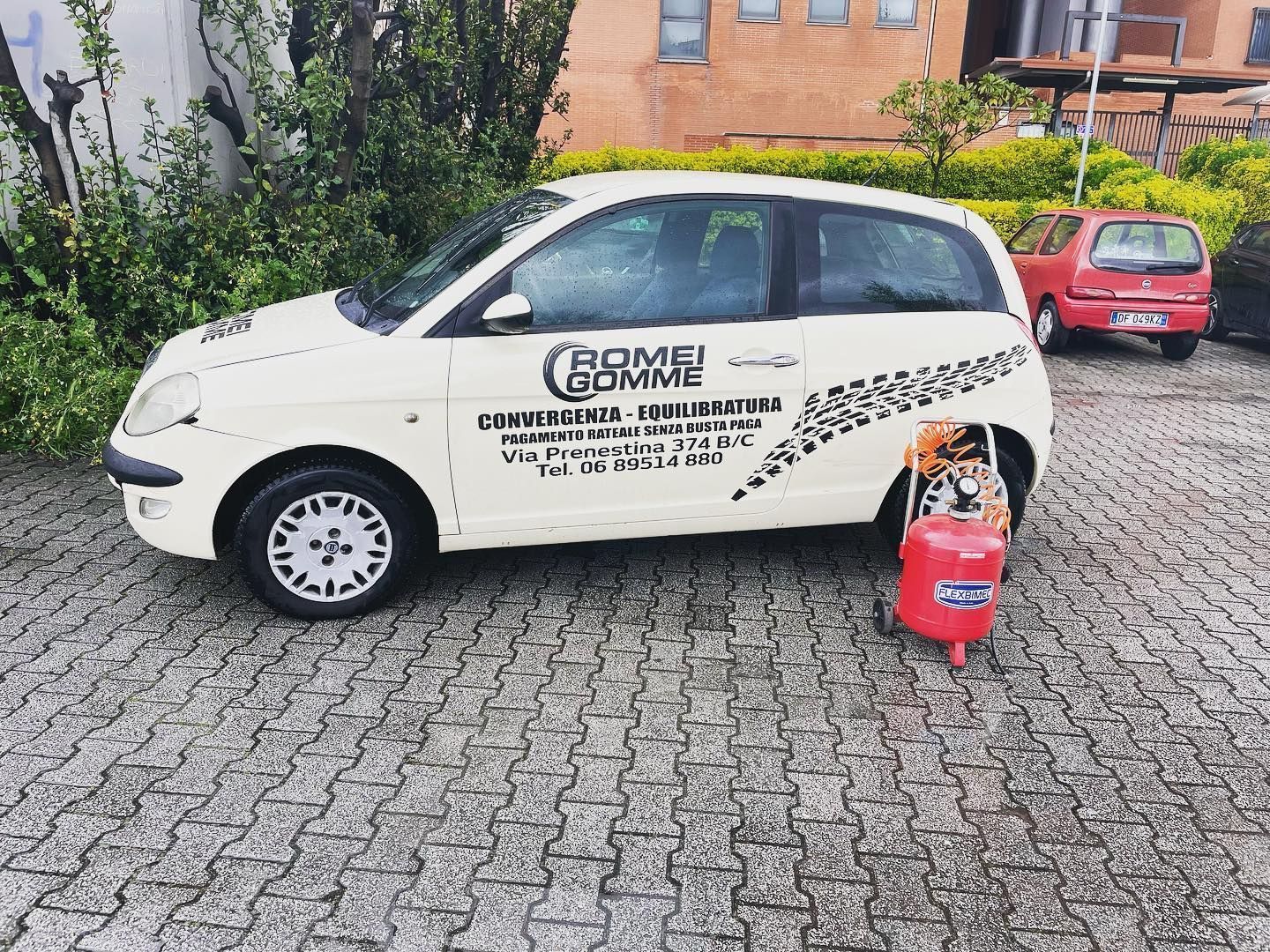 Furgone bianco per le consegne con il logo aziendale parcheggiato su una strada acciottolata accanto a una bombola di gas rossa.