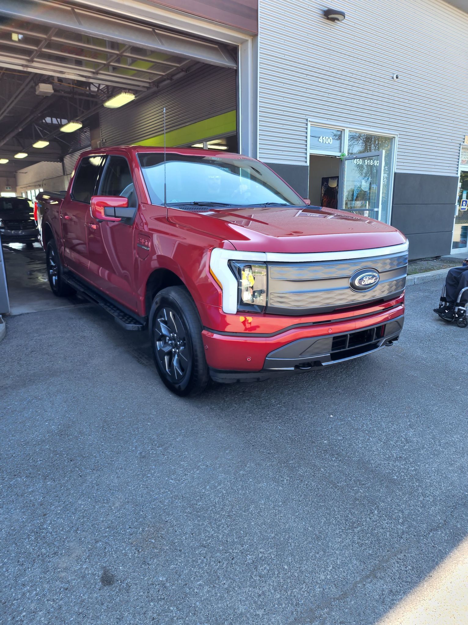 A red ford f150 electric truck is parked in front of a garage.