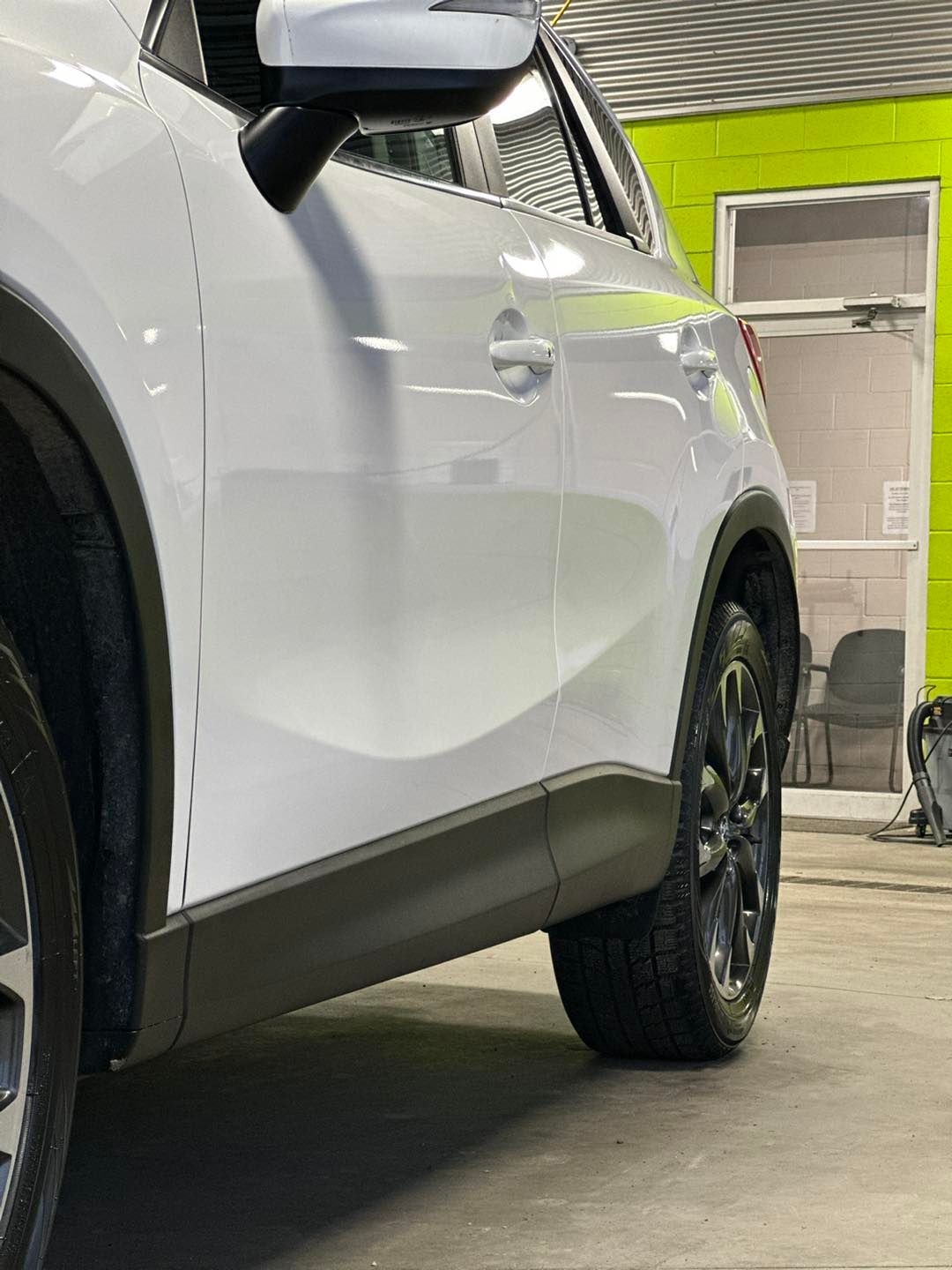 A white car is parked in a garage next to a green wall.