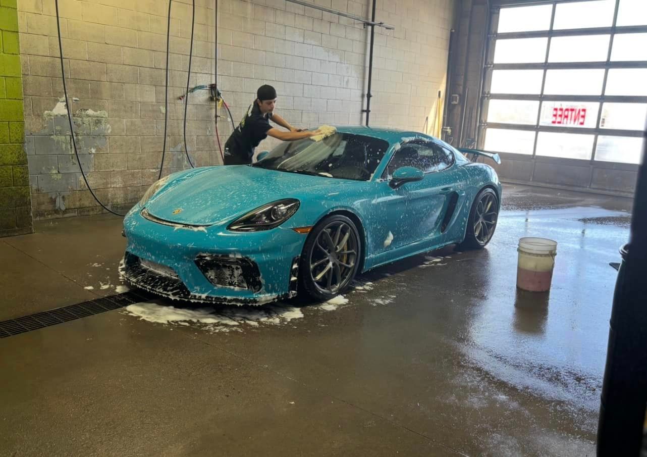A man is washing a blue sports car in a car wash.