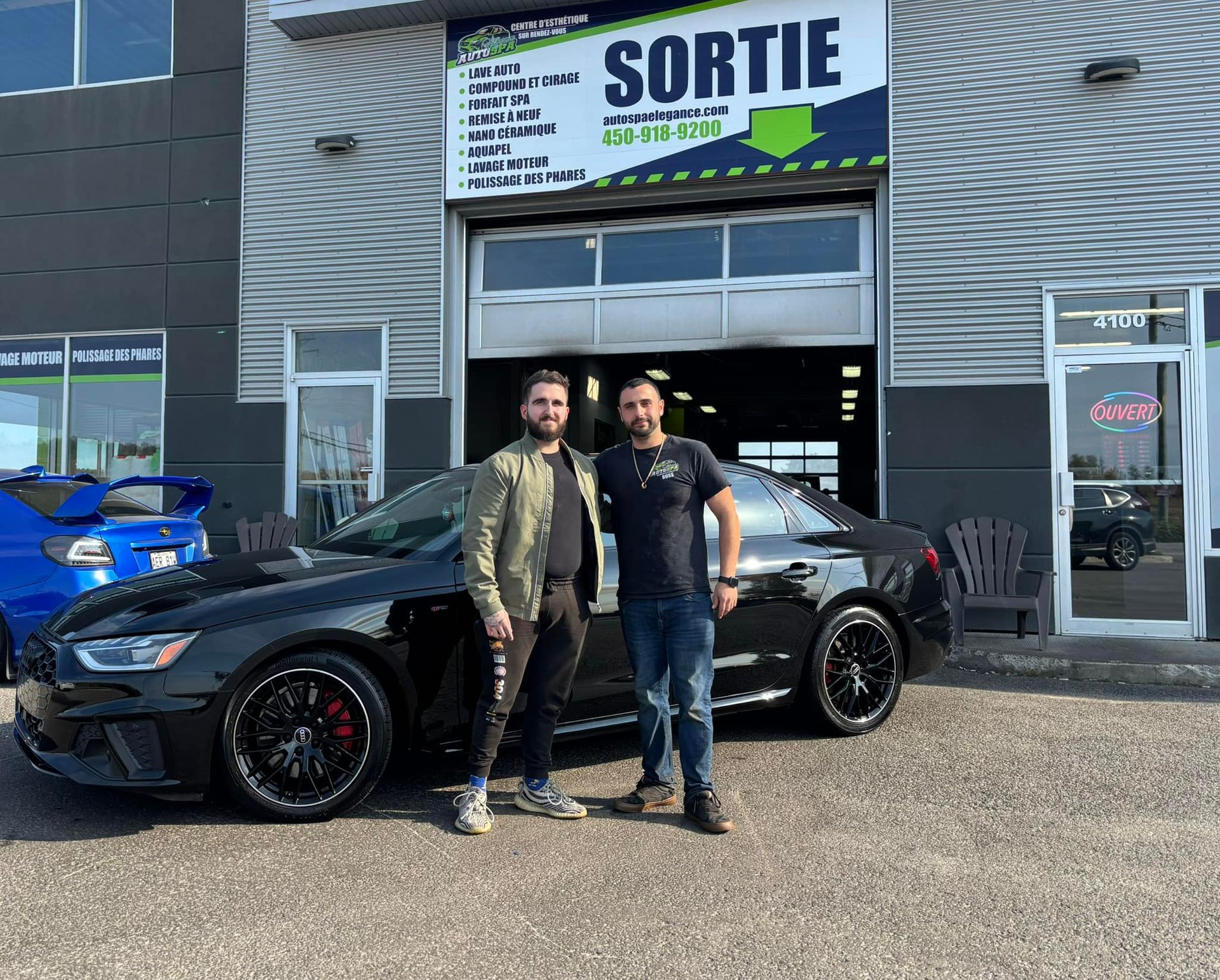 Two men are standing next to a black car in front of a building.
