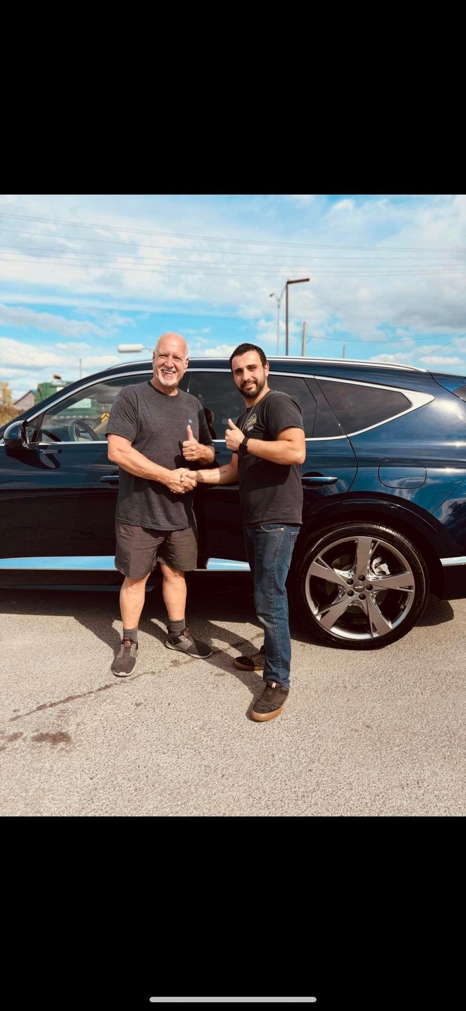 Two men are shaking hands in front of a blue suv.