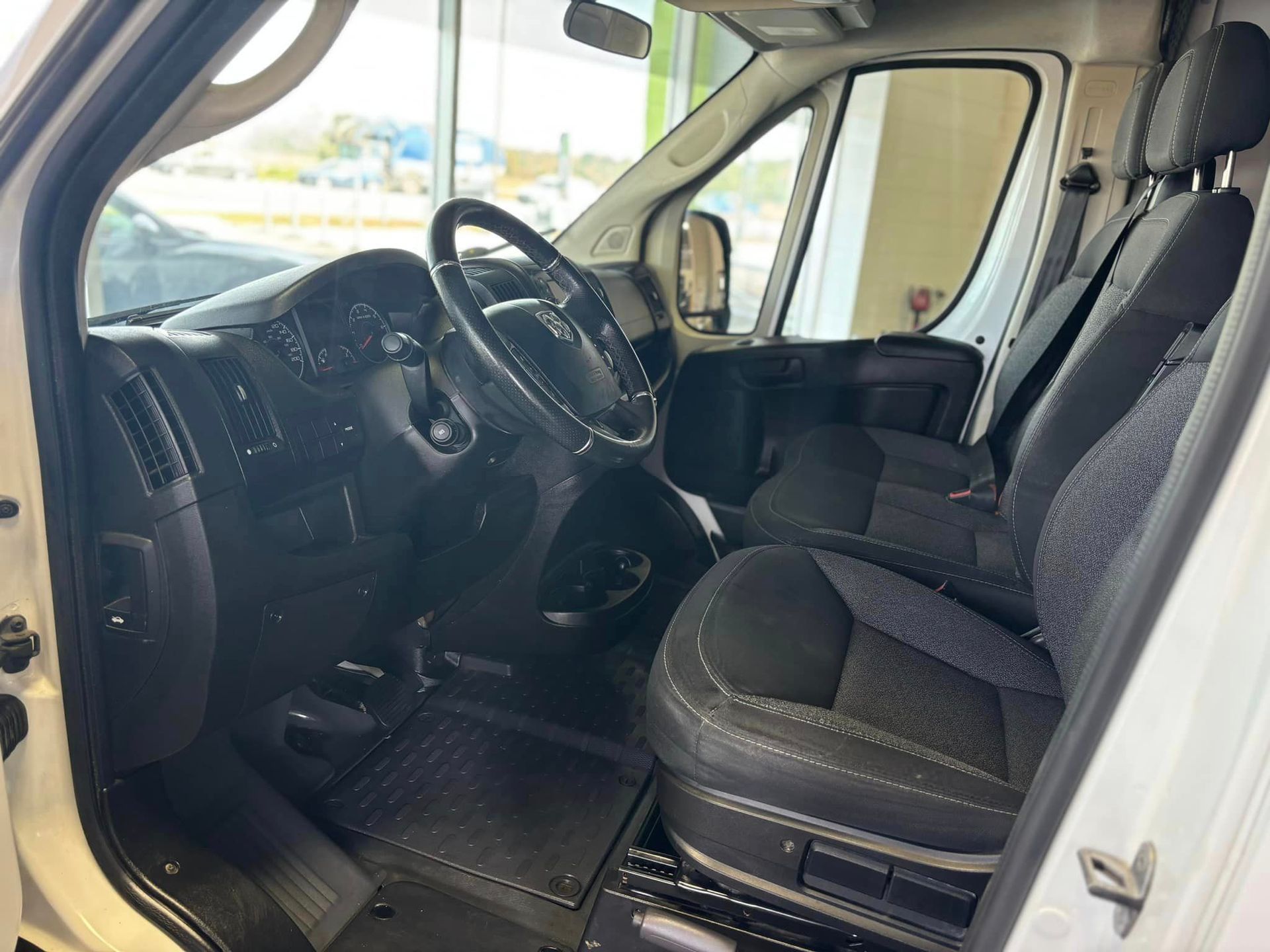 The interior of a white van with black seats and a steering wheel.