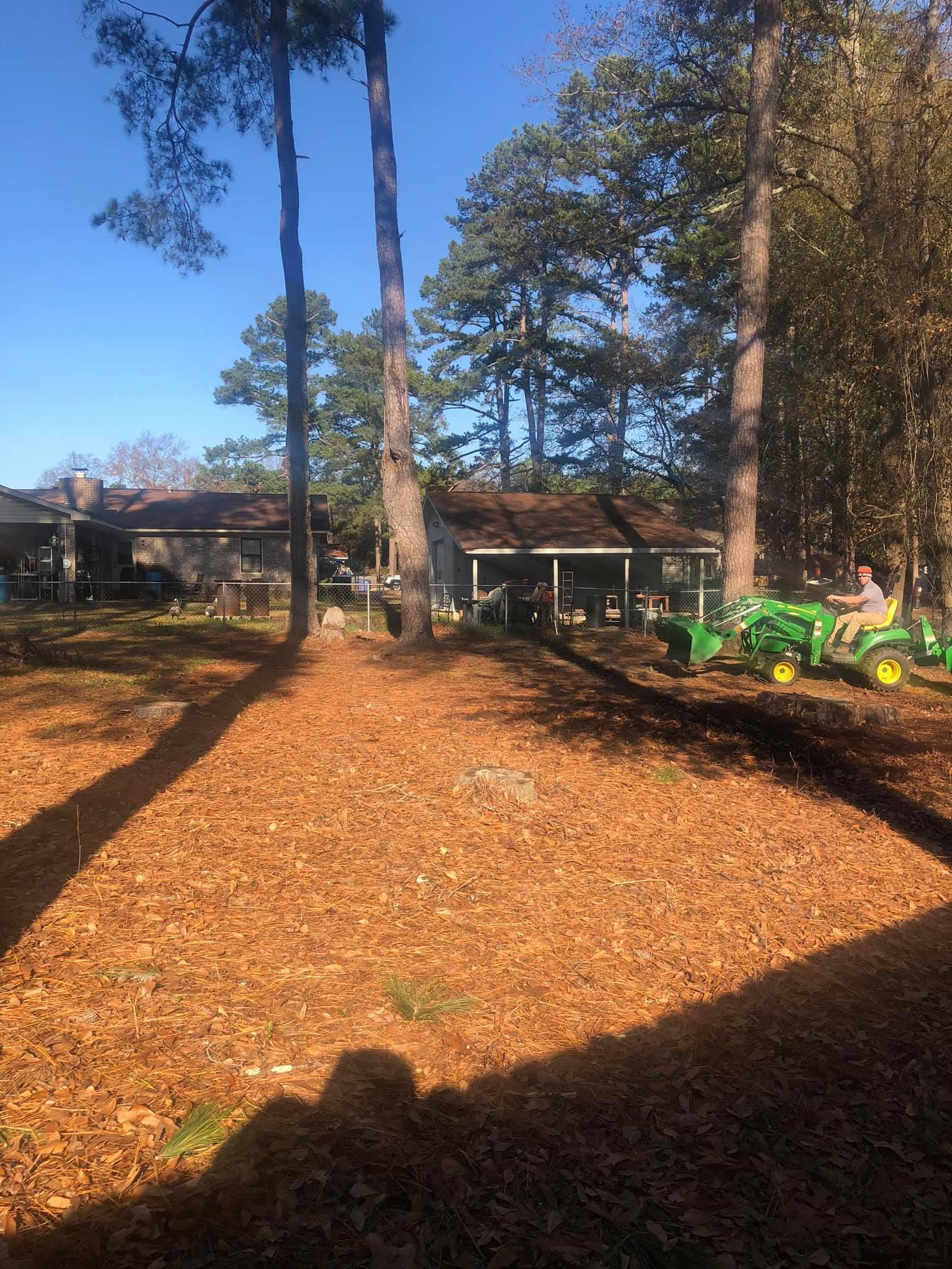 A person drives a green tractor across a large, leaf-covered lawn toward a house with a porch.
