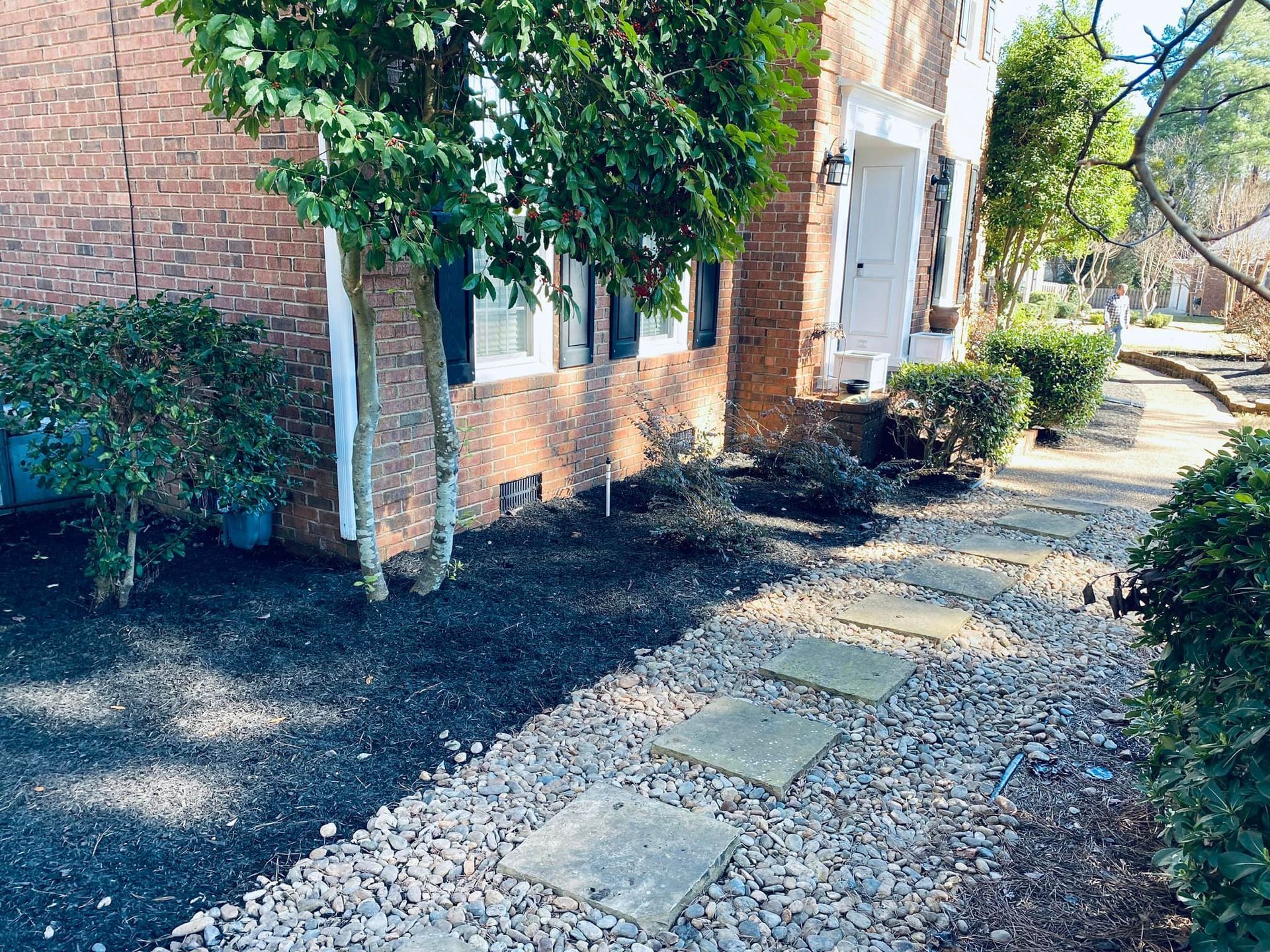 Stone pavers set in a gravel path leading to a front door next to a brick house with dark mulch and green shrubs.