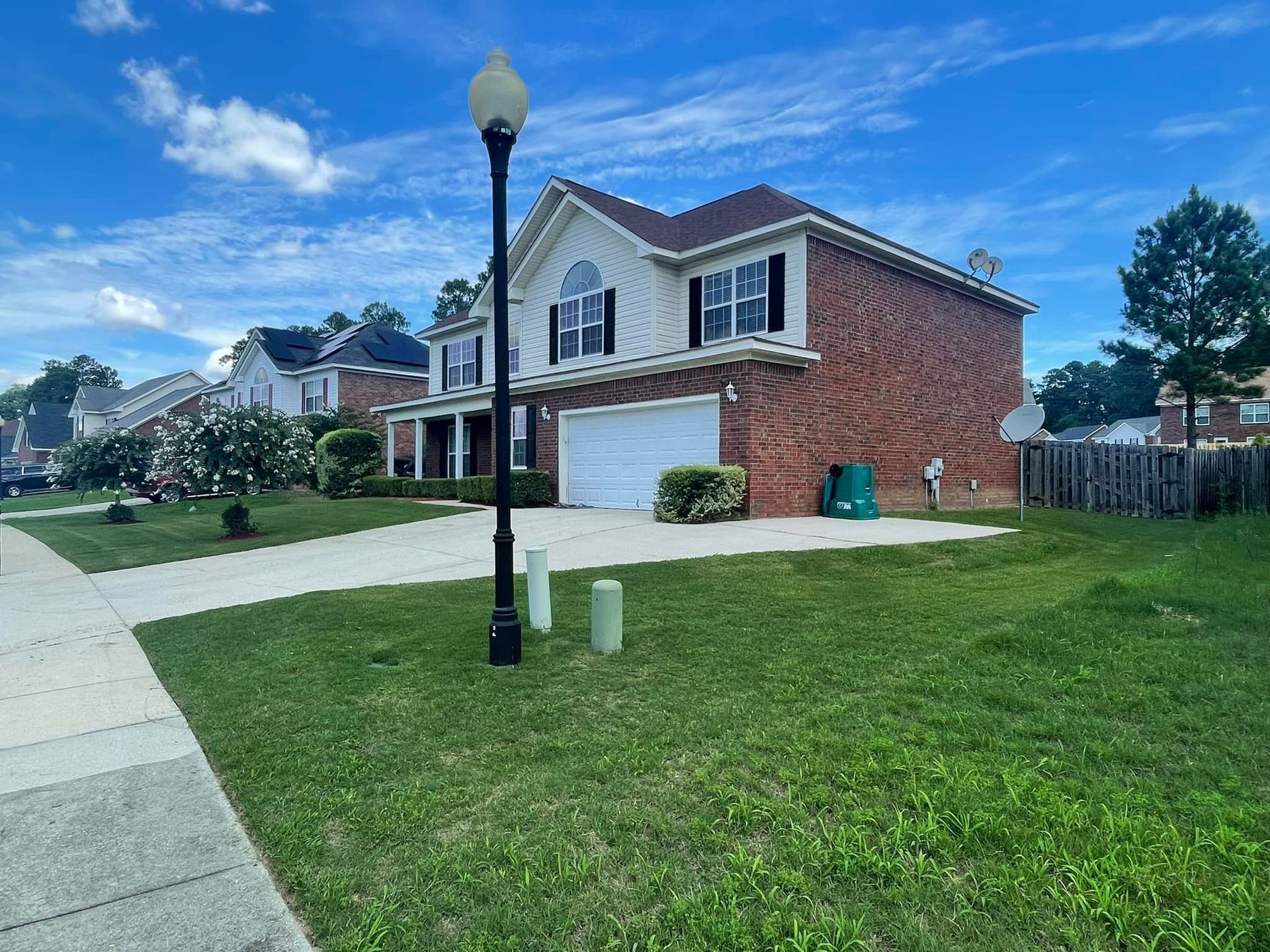 A two-story brick suburban house with a white garage under a bright blue, partly cloudy sky.