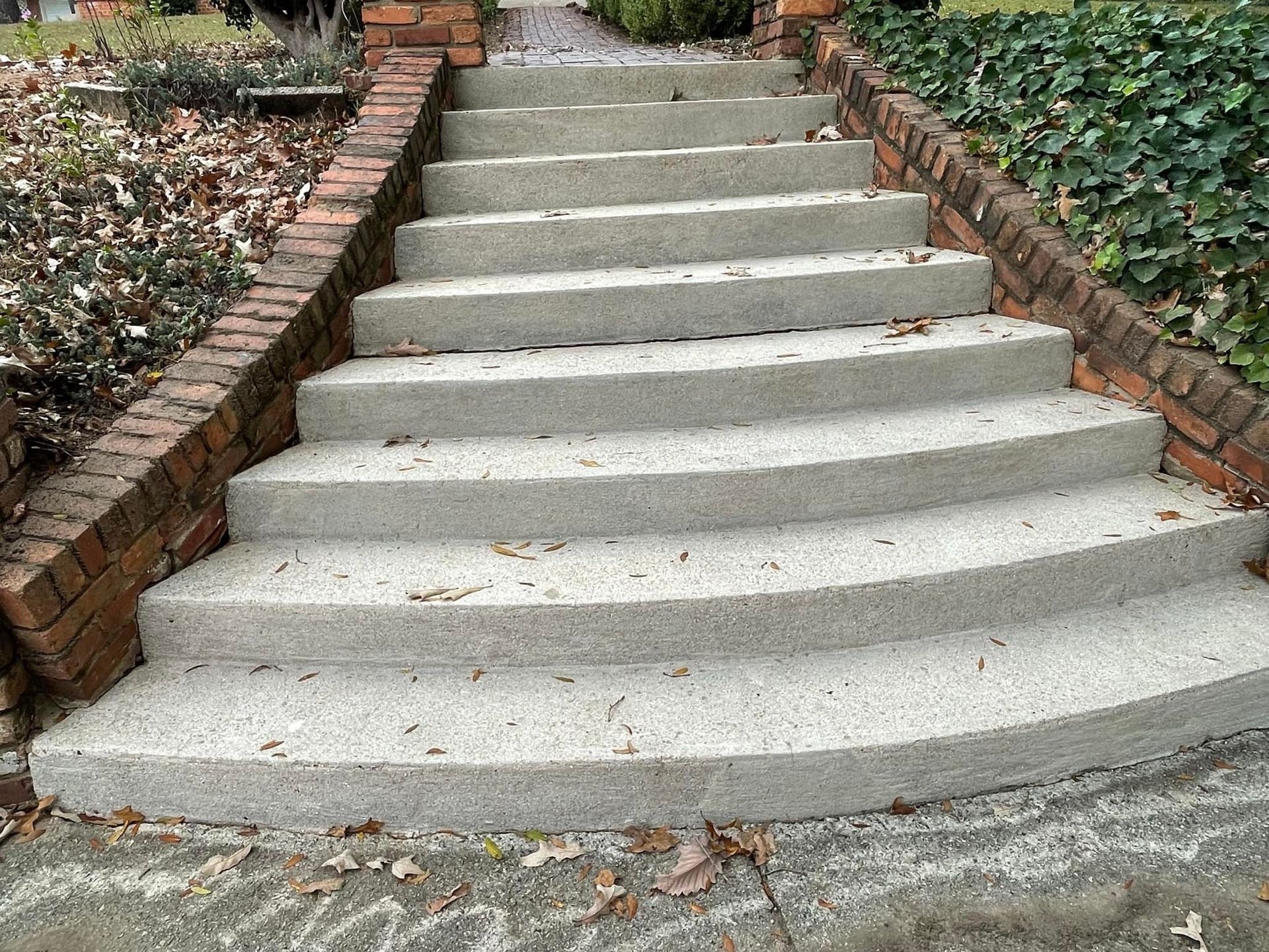 A set of eight concrete outdoor stairs lined with red brick walls, framed by ground cover plants and a paved walkway.