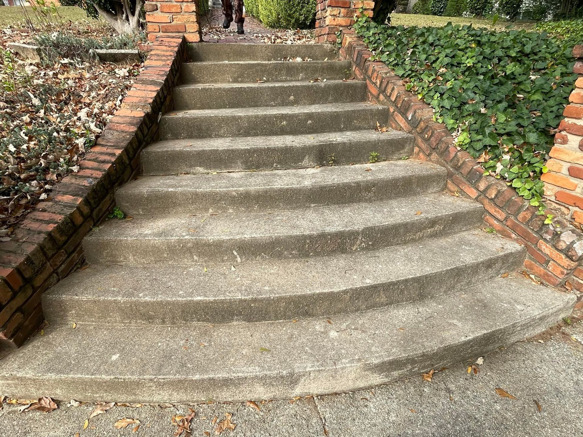 A set of concrete outdoor steps leading upward, flanked by brick retaining walls and greenery.