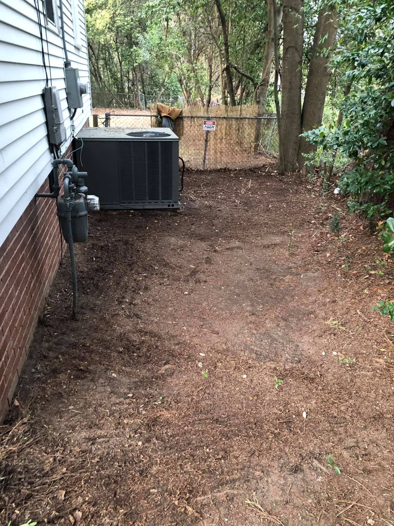 An outdoor view of an HVAC unit sitting on the ground next to a residential brick and siding wall near a wooden fence.