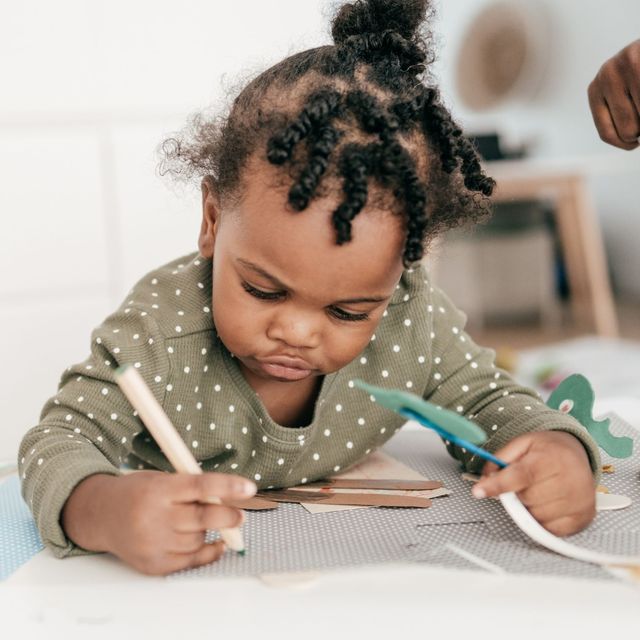 Toddler drawing with colored pencils at a table, focused on a sheet of paper