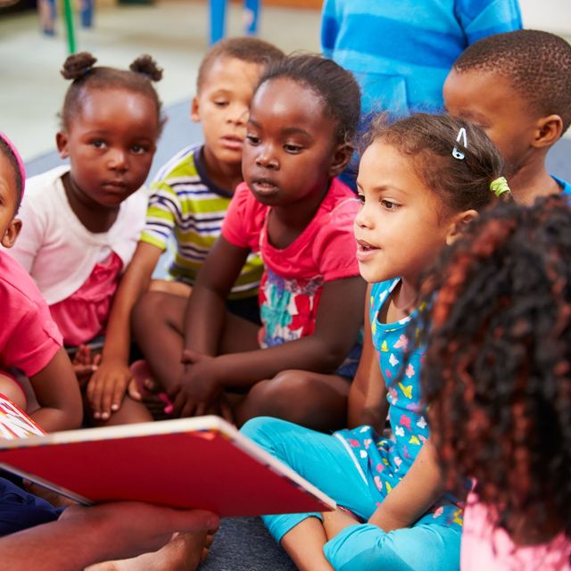Children sitting together listening to a story with a red book in a classroom