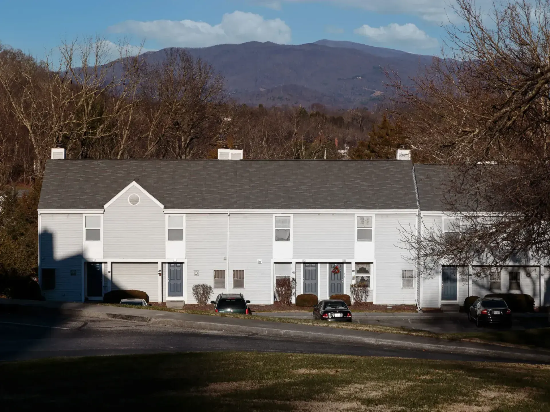 White apartment building with parked cars in front and a mountain backdrop